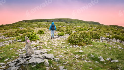 Preview: Man hiking across rocky limestone landscape at The Burren in County Clare Ireland during sunset