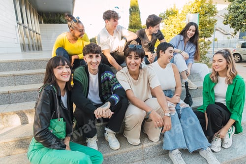 Preview: Cheerful group of diverse friends sitting in daylight on building stairs
