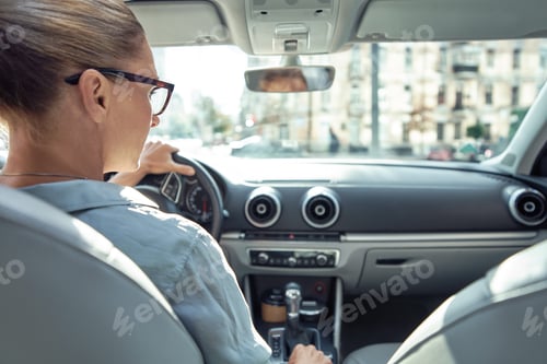 Preview: Rear view of caucasian business woman sitting behind steering wheel of her car, driving safely in
