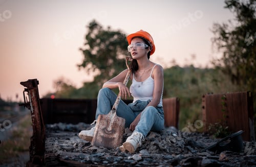 Preview: Beautiful woman coal worker posing tried from work rest by sitting on railway with orange helmet rel