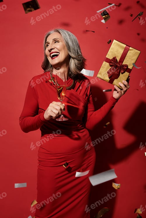Preview: A joyful mature woman with grey hair celebrating New Year's with festive cheer and a gift