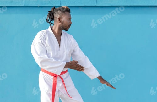 Preview: a young african american man training taekwondo outdoors on a blue background