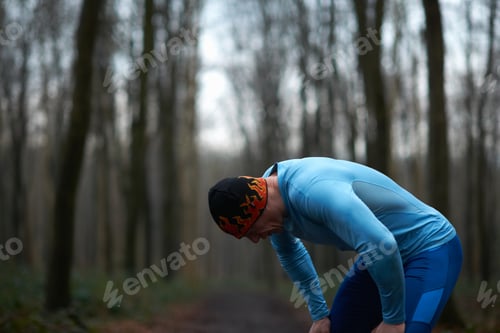 Preview: Runner wearing knit hat and spandex bending forward hands on knees exhausted