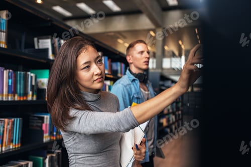 Preview: University students taking book from shelf in library