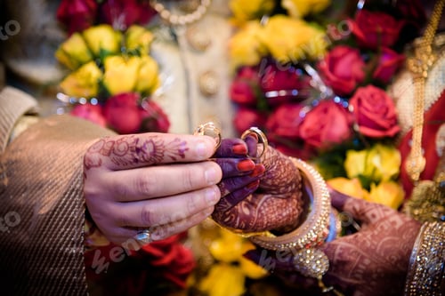 Preview: Shallow focus of an Indian couple with Mehndi on their hands holding wedding rings