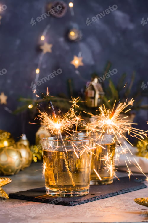 Preview: Gushing sparklers in glasses of drinks on the Christmas table. Gold palette. Vertical view