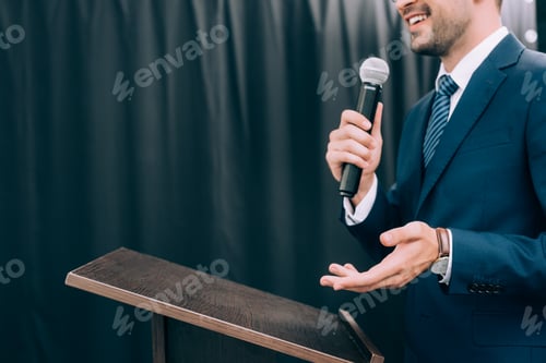 Preview: cropped image of speaker gesturing and talking into microphone at podium tribune during seminar in