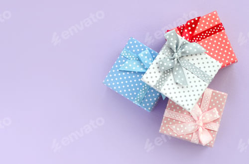 Preview: Pile of a small colored gift boxes with ribbons lies on a violet background