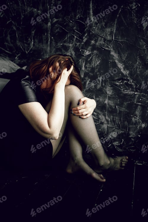 Preview: Young woman sitting in corner, hiding her face and hugging her knees. Mental health.