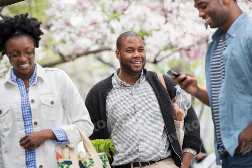 Preview: Three people in a city park in spring, one man checking his phone,