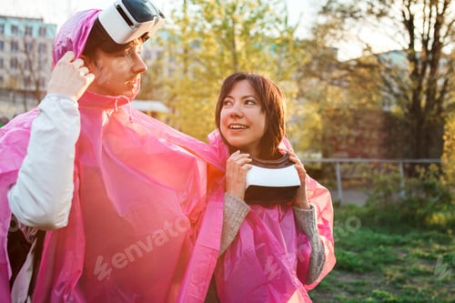 Preview: Closeup shot of a male and a female in pink plastic raincoats and VR headsets taken off