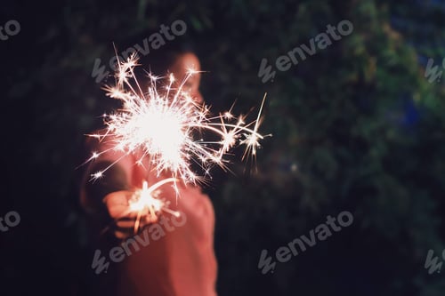 Preview: Woman holding sparkler at night time.