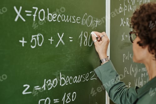 Preview: Young college teacher writing down equation on blackboard at lesson