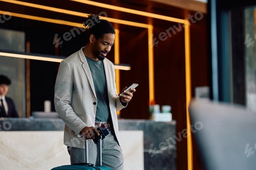 Preview: Happy black man using cell phone in a hotel lobby.