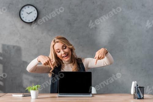 Preview: smiling businesswoman pointing with fingers at laptop with blank screen