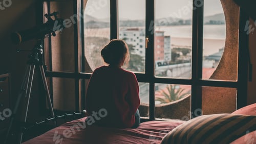 Preview: Girl looking through the window of her room sitting on the bed. In the background is the beach