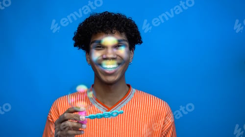Preview: Smiling african american man holding wand near soap bubbles isolated on blue