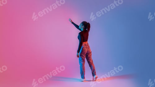 Preview: Back view of young black lady using virtual interface, touching imaginary screen, standing on neon