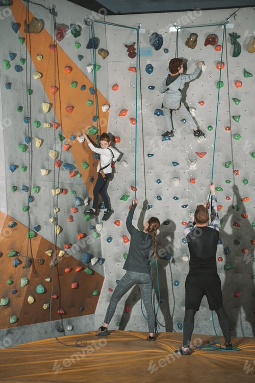 Preview: Full-length shot of two little kids climbing a wall at gym and their mother and father holding