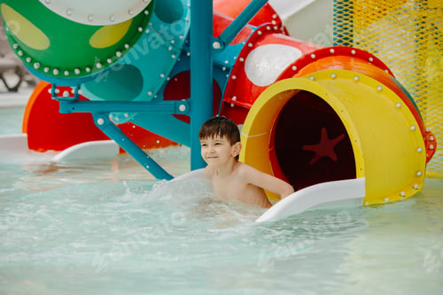 Preview: Happy boy on water slide in pool having fun during summer vacation.