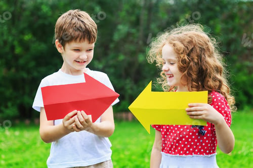 Preview: Children holding color arrow pointing right and left, in summer park. Childhood, frendship concept.