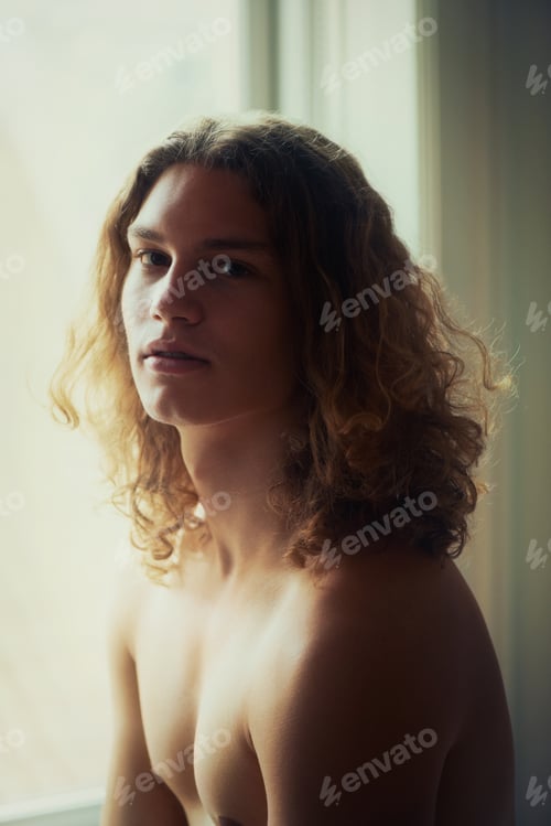 Preview: Touched by the soft window light. Portrait of a young handsome man standing in front of a window.
