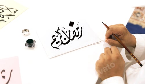 Preview: Handwritten calligraphy greeting on white piece of paper "Ramadan Kareem", hands in frame