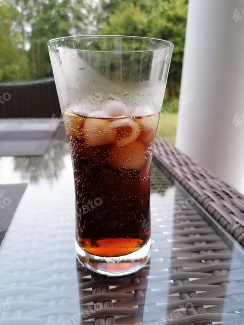 Preview: Vertical shot of a tall glass with iced brown carbonated liquid