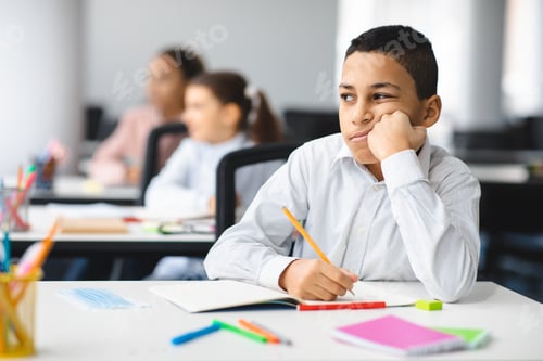 Preview: Bored boy sitting at desk in classroom