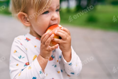 Preview: Little baby is eating a red apple. Close-up