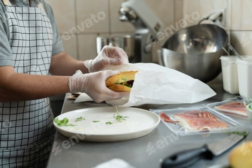 Preview: Unrecognizable man packing prepared sandwich in commercial kitchen