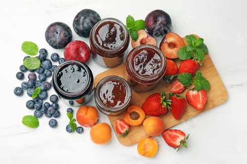 Preview: Different sweet jams in jars and ingredients on white marble table, flat lay