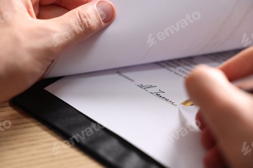 Preview: Man putting signature on document at wooden table, closeup
