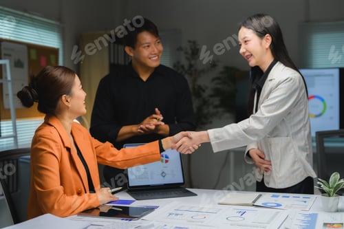 Preview: Asian businesswomen shaking hands over office desk while businessman clapping