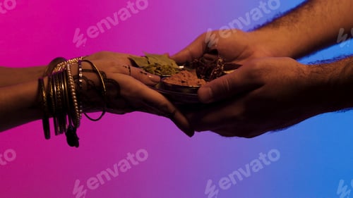 Preview: Man passes a plate of spices to indian woman with many bracelets and mehendi on her hands, isolated