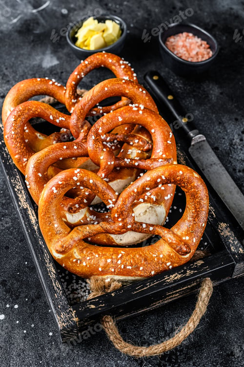 Preview: Bavarian baked Salted pretzels in a wooden tray. Black background. Top view