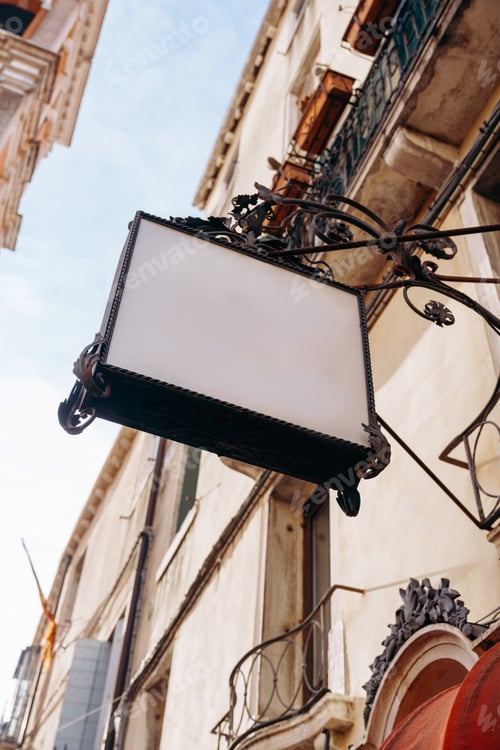 Preview: Sign hanging from a building on a narrow street in a city during daytime