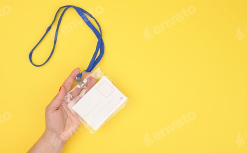 Preview: Female hand holds transparent plastic badge on a blue lanyard on a yellow background