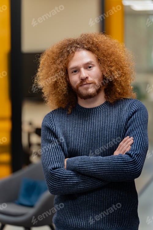Preview: Serious man with curly hair, arms crossed in sweater.