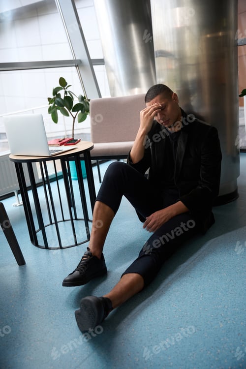 Preview: Depressed man sitting on floor while pressing fingers to forehead