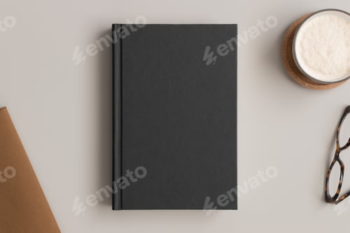 Preview: Black book mockup with a coffee and workspace accessories on a beige table.