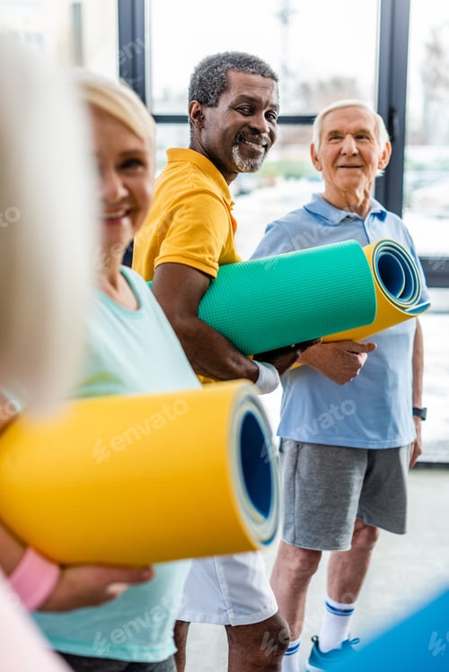 Preview: african american sportsman with fitness mat standing near friends at gym