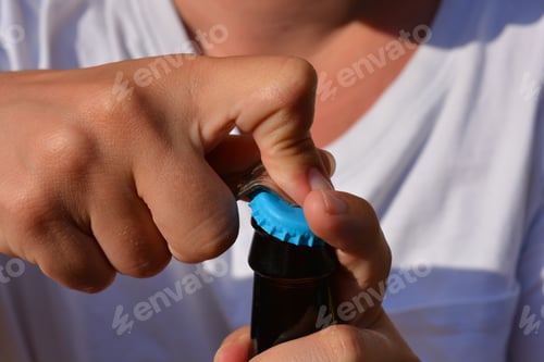 Preview: Young woman using a bottle opener to open a bottle of beer, close up of hands, selective focus