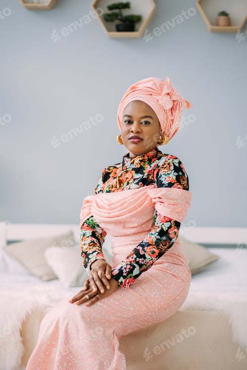 Preview: Young beautiful African lady wearing traditional pink dress and head turban, earrings and makeup