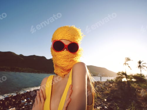 Preview: A woman in a yellow dress, wearing sunglasses and a duck mask, stands by the ocean, creating a