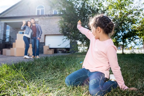 Preview: little girl waving to parents while sitting on grass of new garden