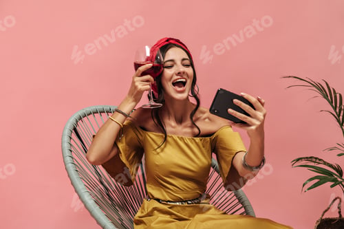 Preview: Happy cute woman with wavy dark hair in red bandana and earrings posing with smartphone and holding