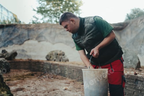 Preview: Caretaker with down syndrome in zoo giving food in animal enclosure. Concept of integration people