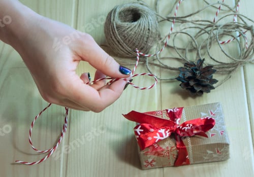 Preview: the girl makes a gift with her own hands, wrapping it in gift paper and tying a bow.