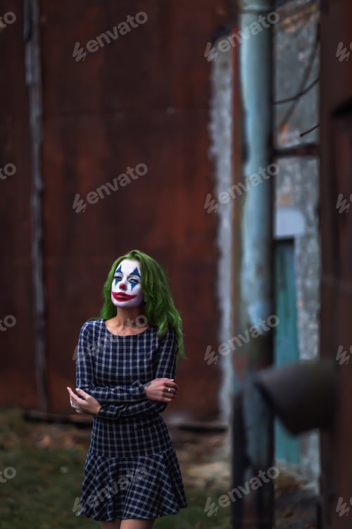 Preview: Portrait of a greenhaired girl in chekered dress with joker makeup on a rusty metal wall background.